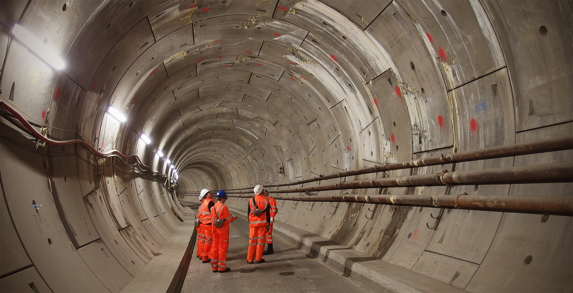 A group of people in orange inspect a tunnel's roof