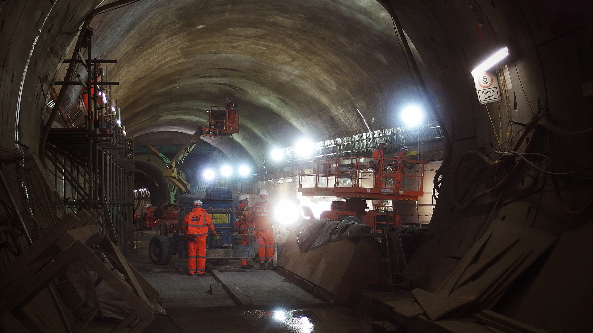 People in orange are working in a large tunnel on an elevated platform