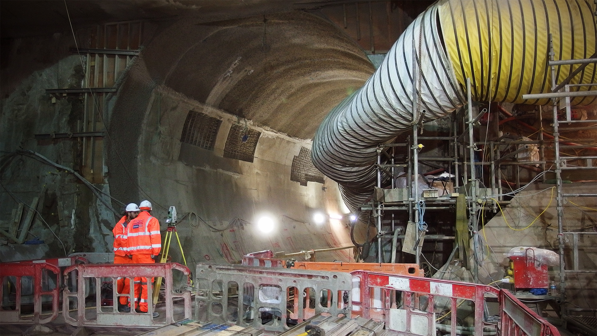 Ventilation tubes feed away from a tunnel, with surveyors working in the tunnel portal