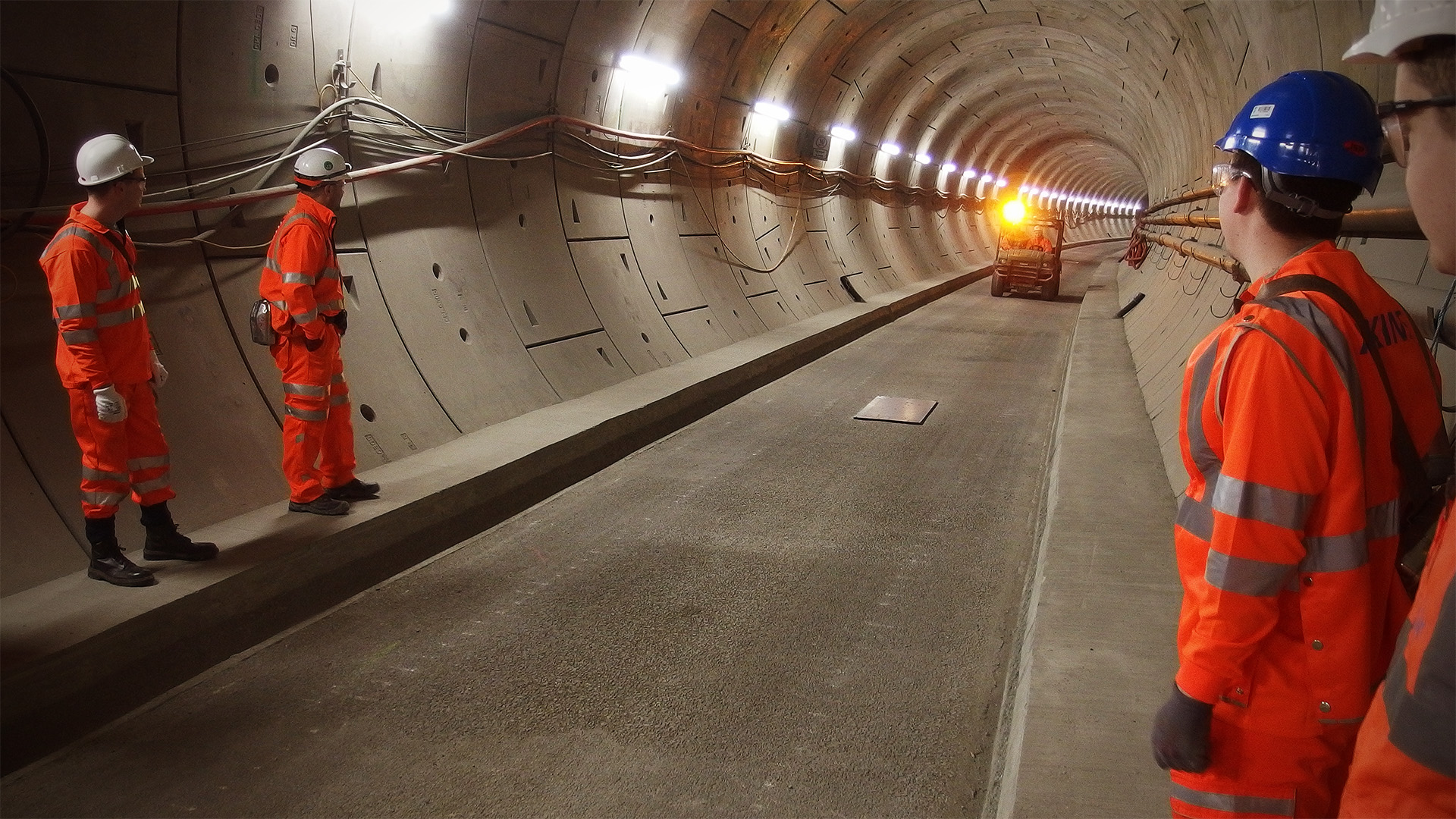 Some people in orange stand to one side to allow the passage of a vehicle