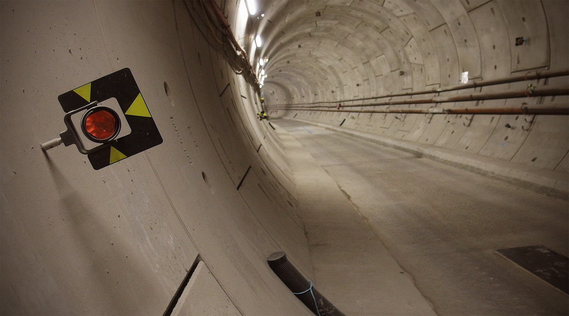 A survey marker with a red prism is mounted on the tunnel wall, with others behind it