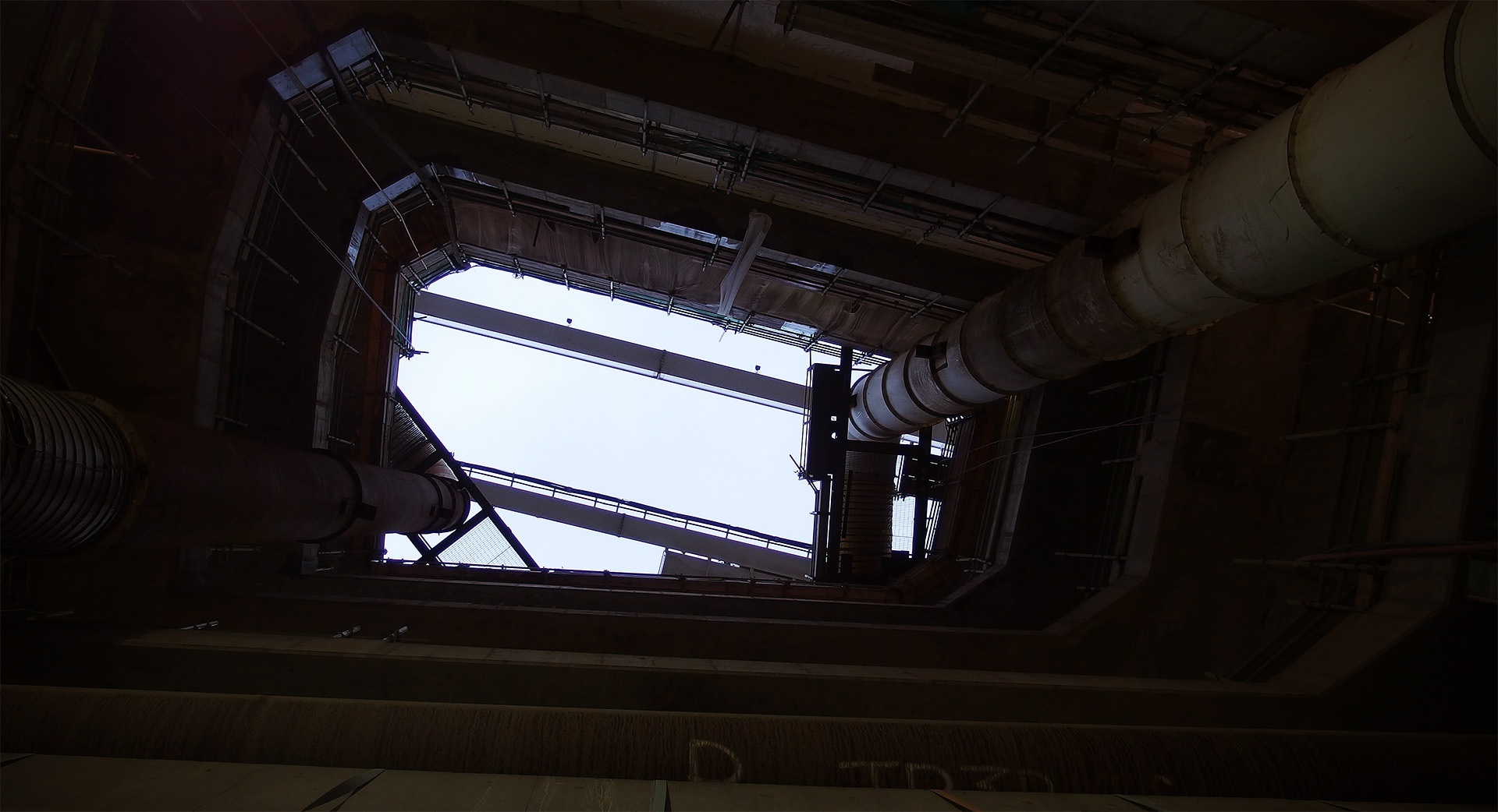 A bright sky is visible above a massive concrete shaft